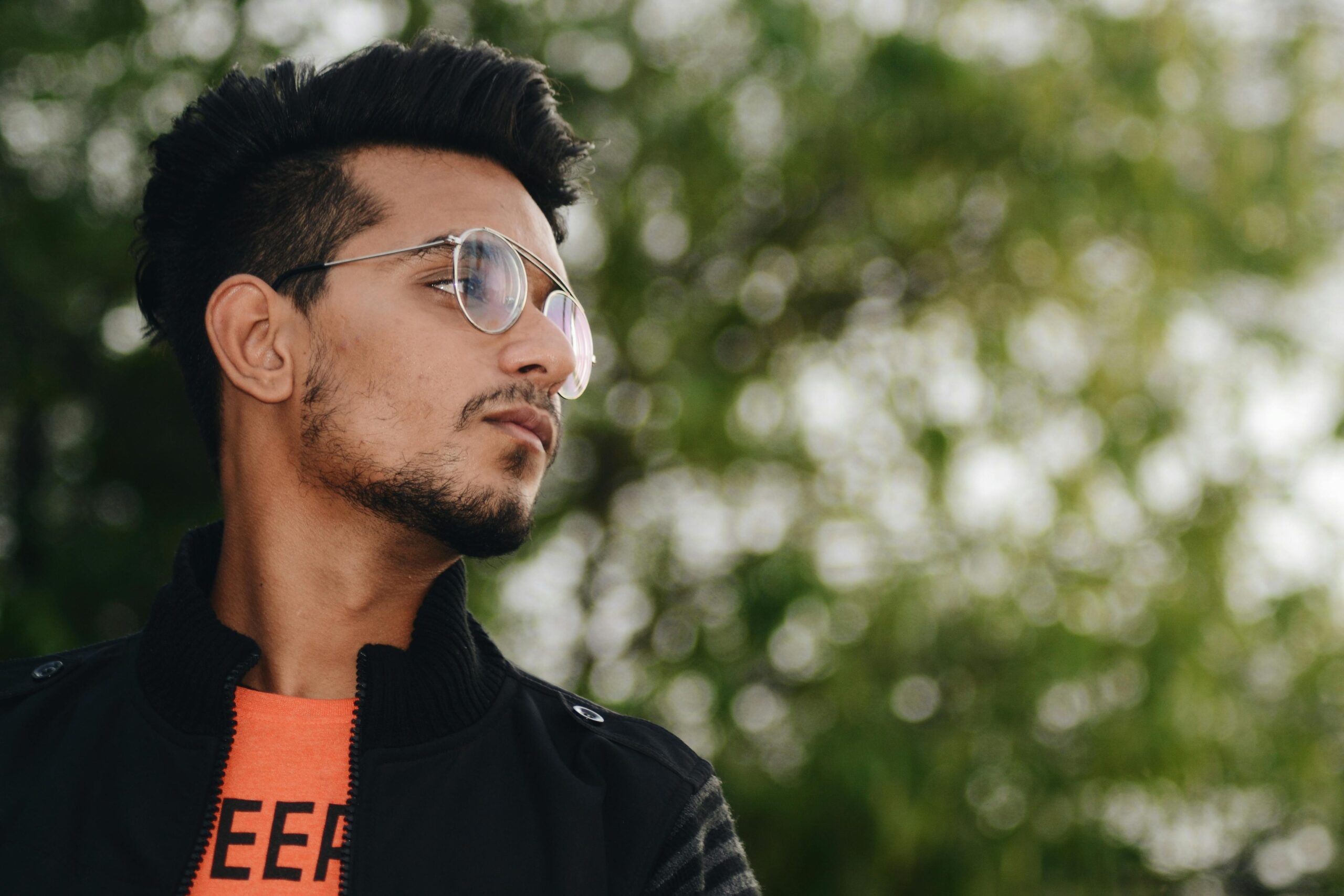 Portrait of a fashionable young man wearing glasses and a jacket outdoors with a natural bokeh background.