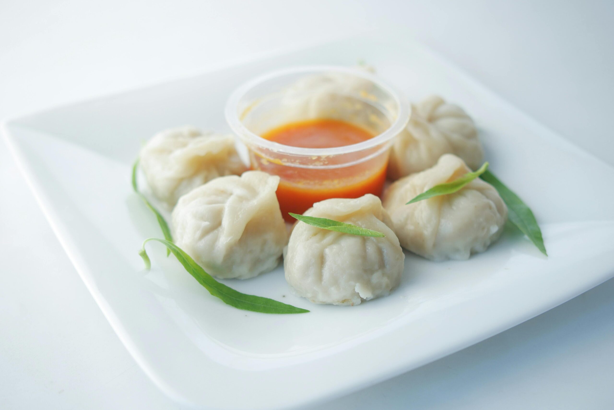 A close-up of delicious steamed dumplings served with spicy sauce on a white plate.