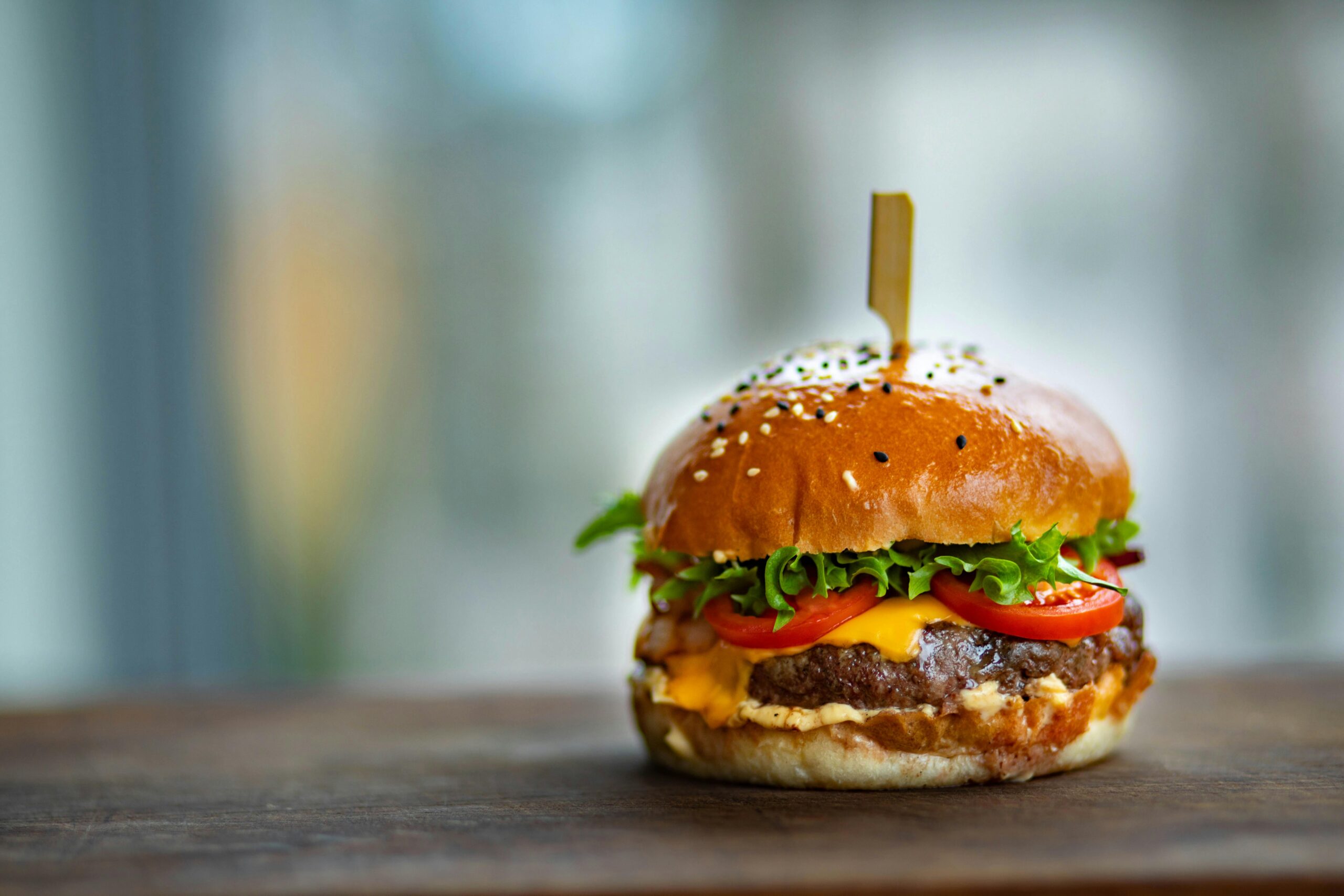 Mouthwatering cheeseburger with fresh tomatoes and lettuce on a wooden surface.