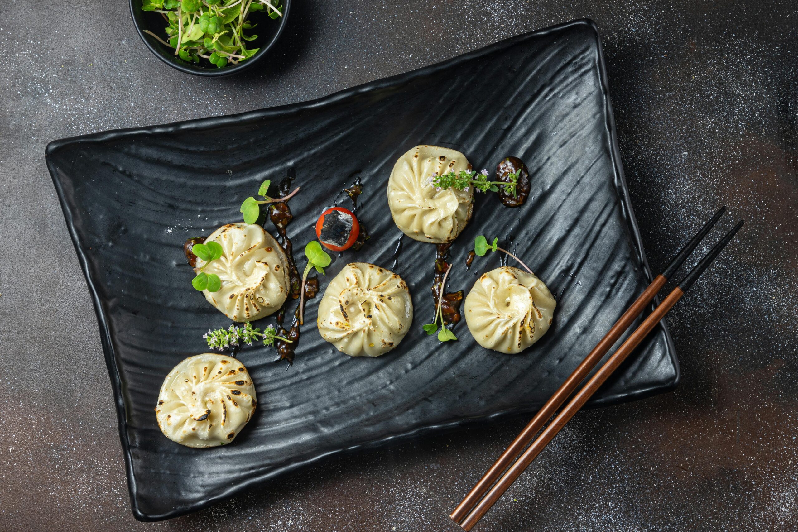 Delicious steamed dumplings garnished with fresh microgreens on a black plate, perfect for food photography.