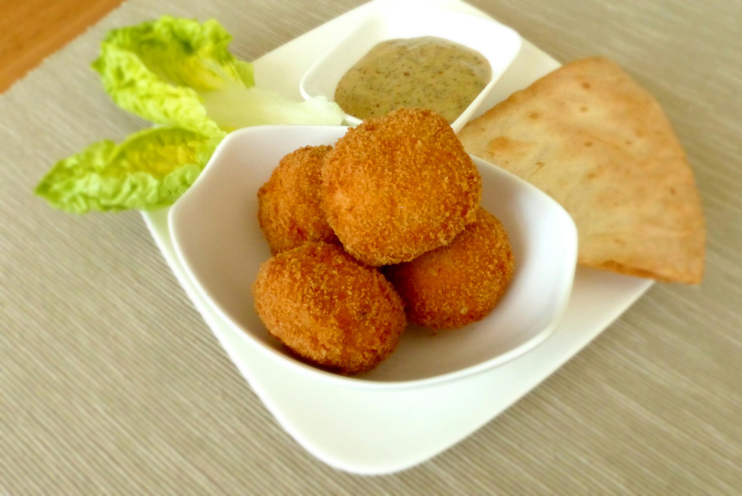 A delicious plate of crispy chicken bites served with sauce, crispy bread, and fresh lettuce.